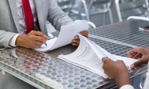 Business partners checking and signing documents in street cafe. Closeup of papers and writing business man hand. Deal or paperwork concept