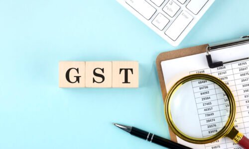 GST word on wooden cubes on a blue background with chart and keyboard