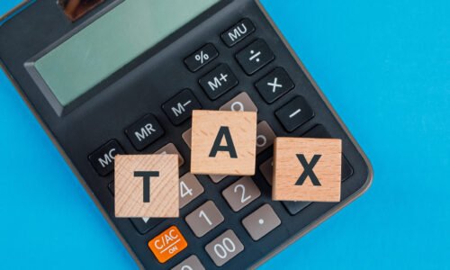 Tax planning concept with wooden cubes on calculator on blue background flat lay.