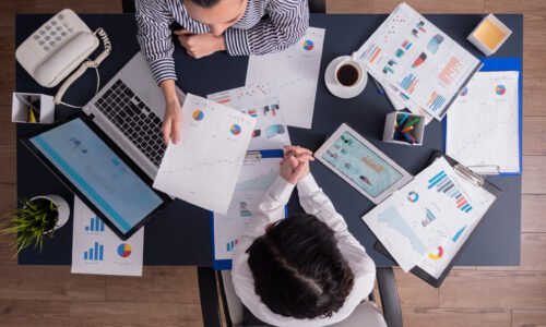 Top view of office workers meeting analyzing financial charts holding clipboard. Manager and employer discussing marketing strategy during briefing. Pointing at graphs.