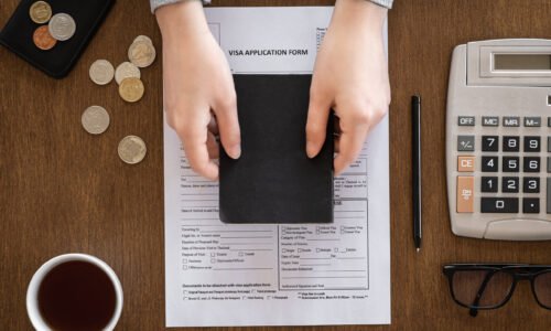 Visa application form, passport in female hands, coins, calculator, coffee on a wooden background, flat lay, visa processing, immigration.