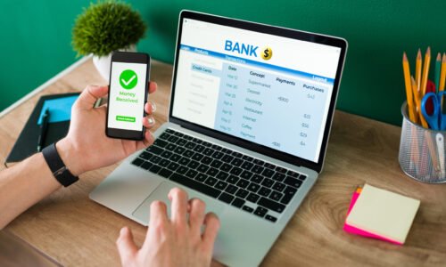 Wire transfer. Young man using his smartphone and laptop to do a banking transaction and some payments